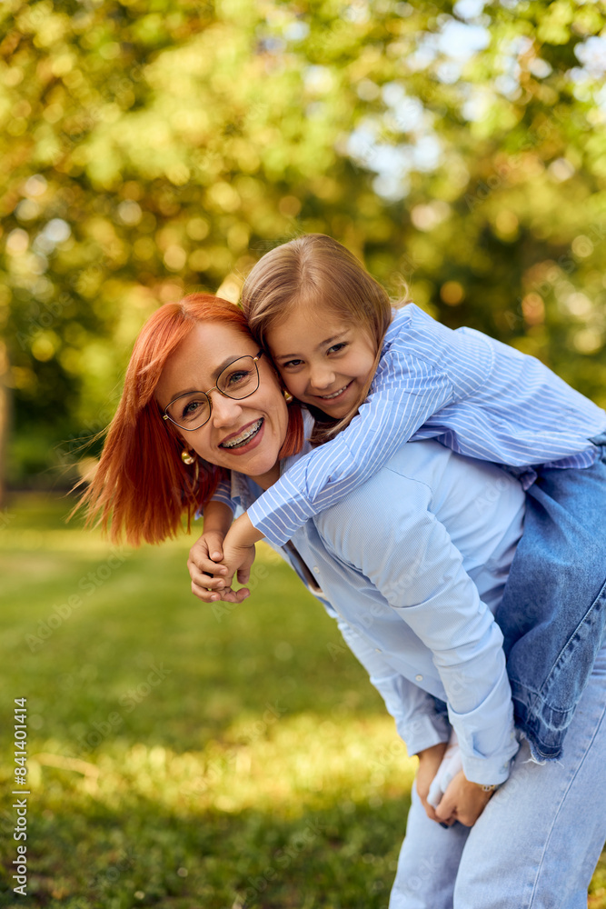 Portrait of a happy mother and daughter, holding her on the back, posing for the camera in the park. Portrait of a happy mother and daughter, holding her on the back, posing for the camera in the park.