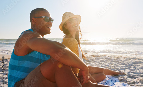 Couple, picnic and happy at beach with sunglasses, sunset and relax for vacation by ocean in summer. Man, woman and smile on sand in California with sky, sun and partner on date for holiday or love