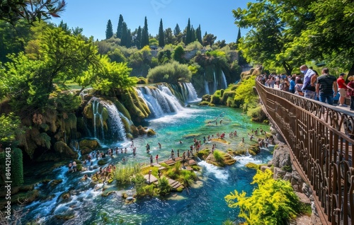 During a bright sunny day, tourists admire the beauty of Upper Duden waterfall from a cave nearby. The landscape is a riot of green vegetation and dense bushes.