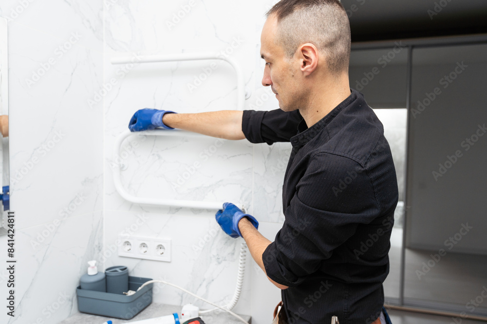 A worker is installing a heating element in the towel warmer in the bathroom. A worker is installing a heating element in the towel warmer in the bathroom.