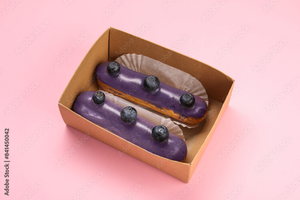 Delicious eclairs decorated with blueberries on pink background