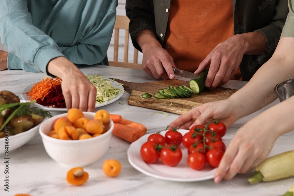 Friends cooking healthy vegetarian meal at white marble table in kitchen, closeup