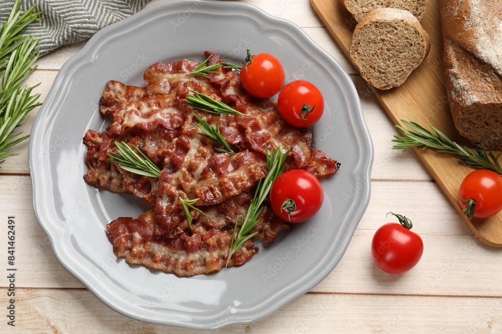 Slices of tasty fried bacon with rosemary and tomatoes served on wooden table, flat lay