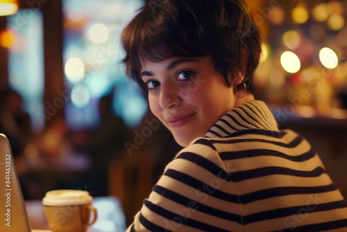 Young woman happily working on her laptop in a cozy cafe, enjoying a warm drink and the urban atmosphere around her