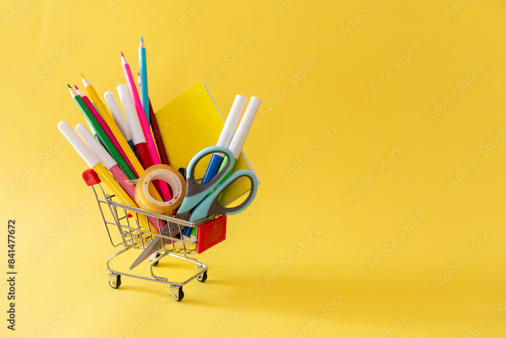 School and office supplies in shopping cart on yellow background School and office supplies in shopping cart on yellow background