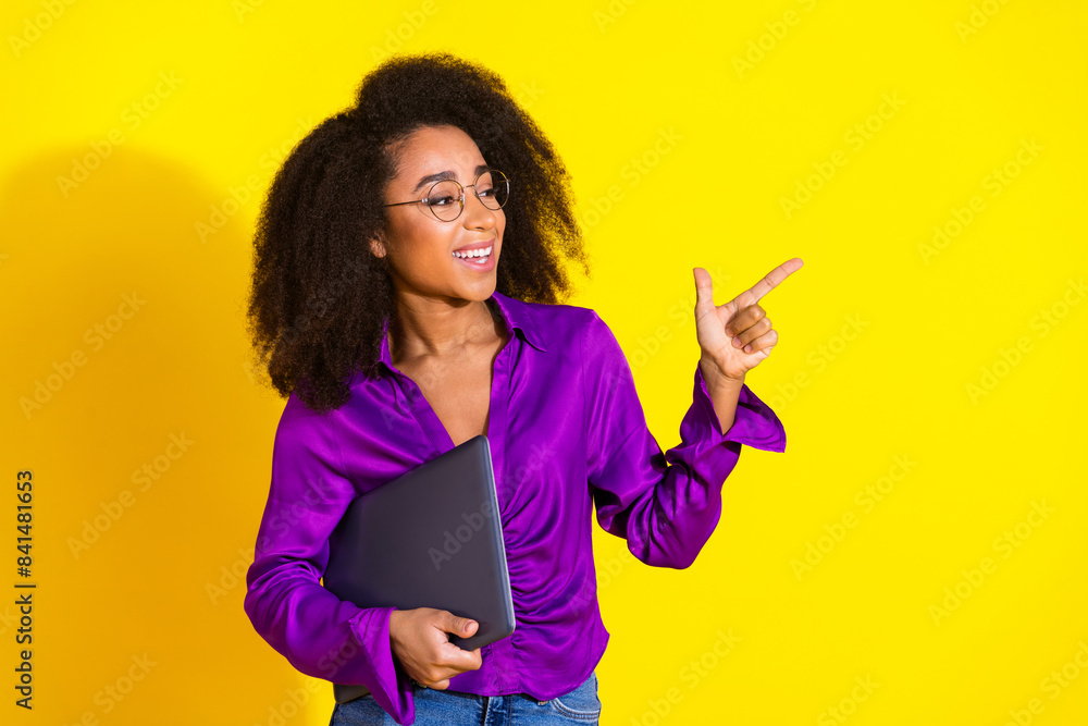 Photo portrait of attractive young woman point empty space hold netbook dressed stylish violet clothes isolated on yellow color background Photo portrait of attractive young woman point empty space hold netbook dressed stylish violet clothes isolated on yellow color background