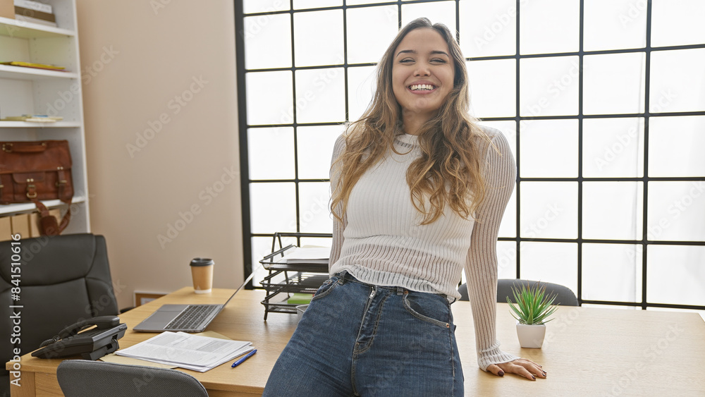 Confident and beautiful hispanic businesswoman enjoying her success - a portrait of a young, smiling office worker, sitting relaxed at the office table, indoors, exuding positive vibes Confident and beautiful hispanic businesswoman enjoying her success - a portrait of a young, smiling office worker, sitting relaxed at the office table, indoors, exuding positive vibes
