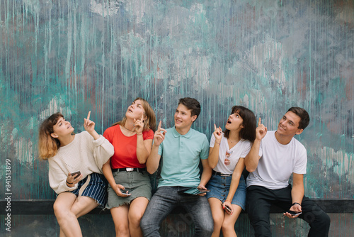 Happy group teenagers show something on the blue wall background with copy space