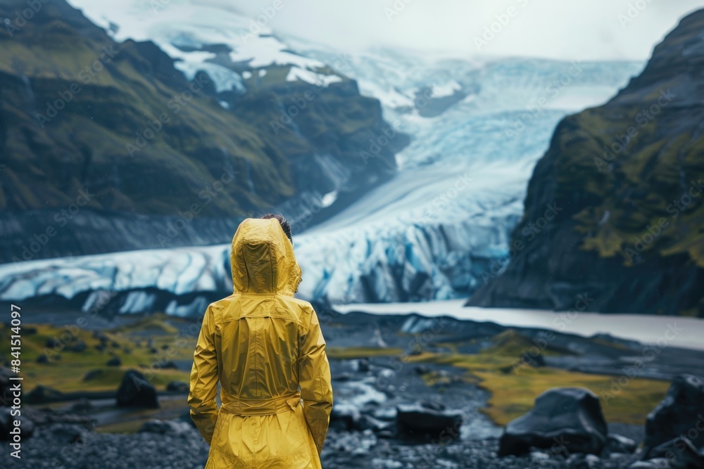 A person in a yellow raincoat standing by a glacier, looking out at the icy landscape A person in a yellow raincoat standing by a glacier, looking out at the icy landscape