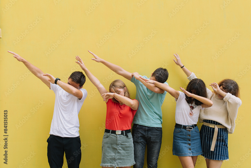 Fototapeta premium Summer holidays and teenage concept - group of smiling teenagers cover their faces with their hands on a yellow wall background