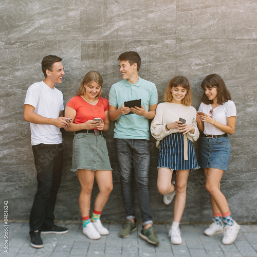 Photography Group of teenagers sitting at the colored wall and using their mobile phones and