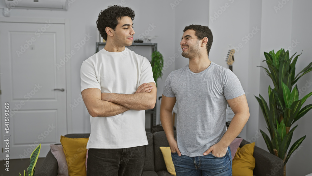 Fototapeta premium Two men smiling and conversing comfortably in a cozy modern living room with decor and plants.