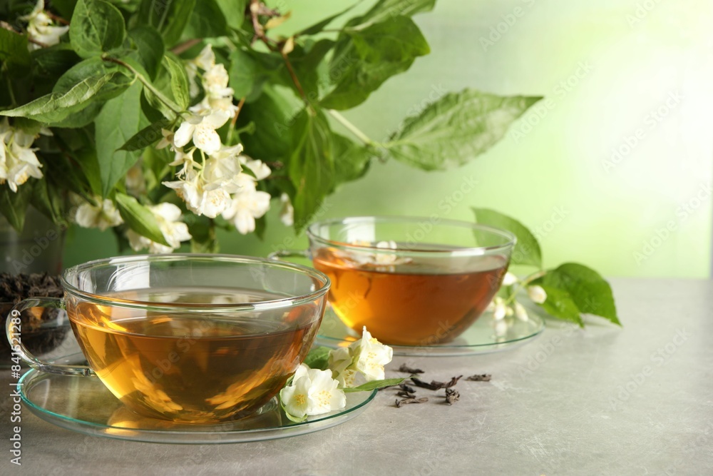 Aromatic jasmine tea in cups, flowers and green leaves on light grey table Aromatic jasmine tea in cups, flowers and green leaves on light grey table