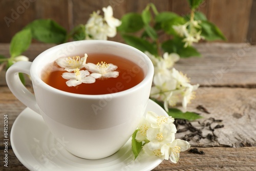 Aromatic jasmine tea in cup, flowers and dry leaves on wooden table
