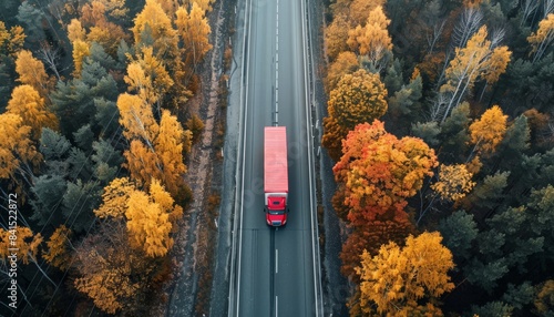A red semi truck drives through a fall forest on a rural road.  Autumn logistics and transportation.