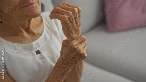 Obraz na plátně Elderly woman in a home, clutching her wrist while sitting on a sofa, displaying signs of aging and discomfort