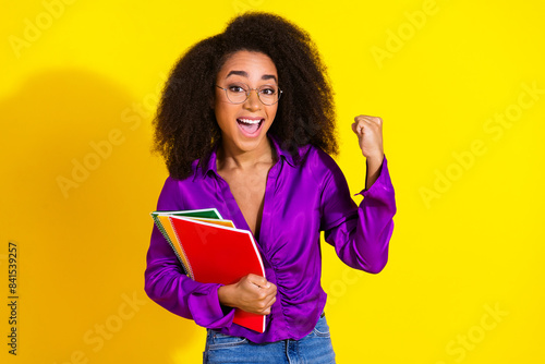 Photo portrait of lovely young lady winning hold copybooks dressed stylish violet garment isolated on yellow color background