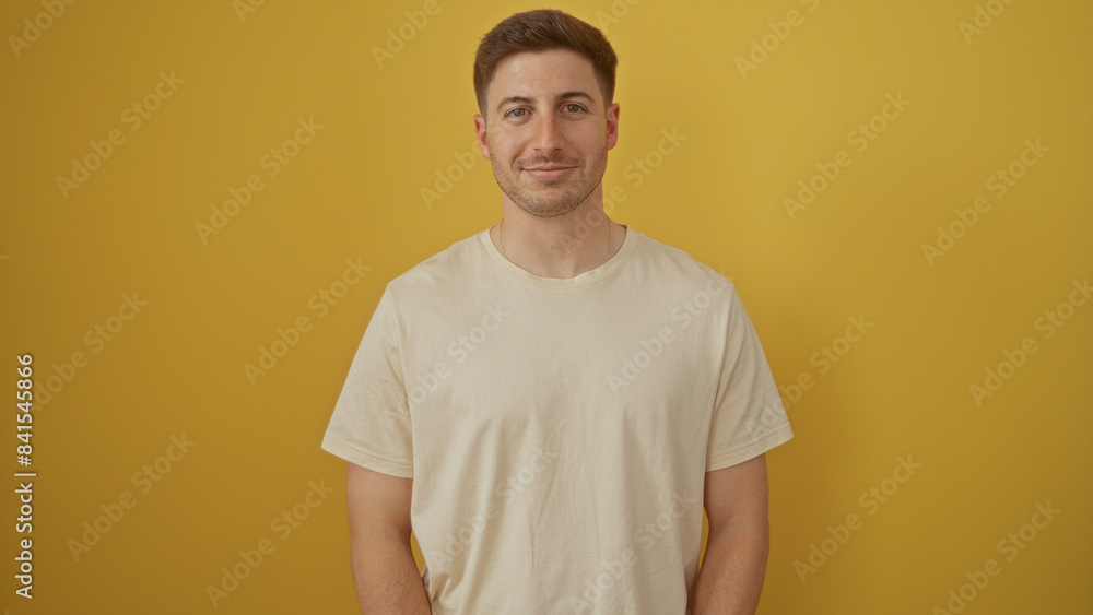 A handsome, young hispanic man is posing against an isolated yellow background, captured in an attractive portrait over a vibrant yellow wall. A handsome, young hispanic man is posing against an isolated yellow background, captured in an attractive portrait over a vibrant yellow wall.