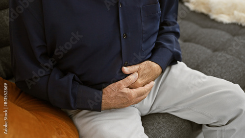 Senior man touching his aching stomach, suffering in pain at home, worriedly resting in the indoor sunlight © Krakenimages.com