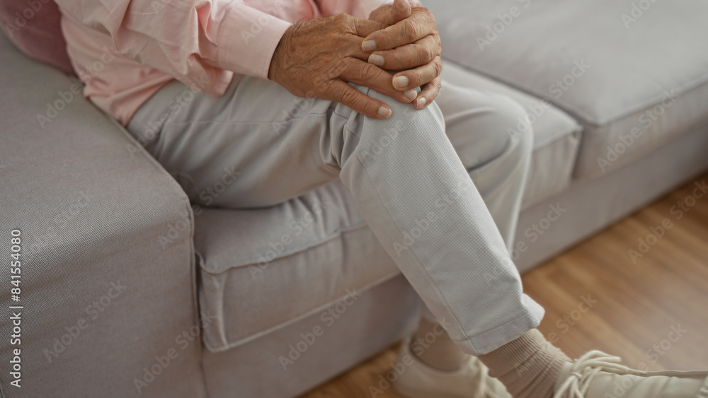 A middle-aged man sits in a cozy living room, his hands clasped on his knee, giving a sense of comfort and relaxation indoors. A middle-aged man sits in a cozy living room, his hands clasped on his knee, giving a sense of comfort and relaxation indoors.