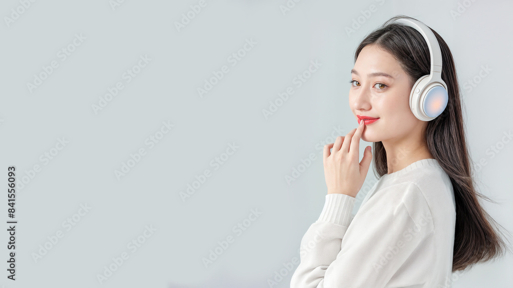 A beautiful young Asian woman with long brown hair wearing headphones, isolated on gray background. Copy space, 16:9 A beautiful young Asian woman with long brown hair wearing headphones, isolated on gray background. Copy space, 16:9