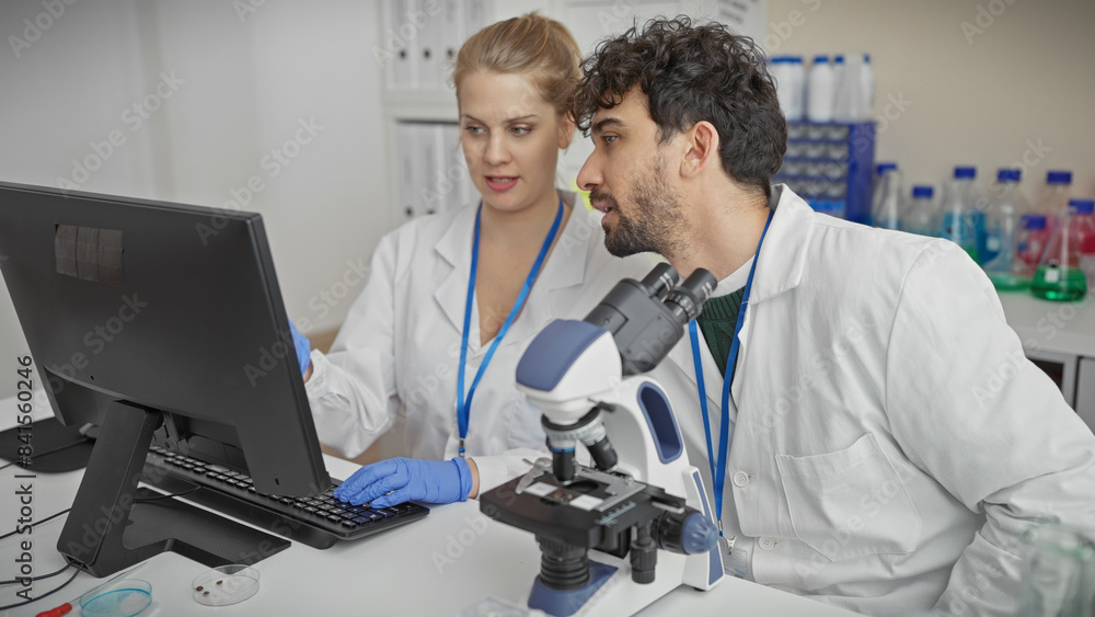 A man and woman in lab coats analyzing data on a computer in a modern laboratory setting. A man and woman in lab coats analyzing data on a computer in a modern laboratory setting.
