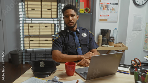 Fotografía Handsome african american male police officer working on laptop in an office with evidence board