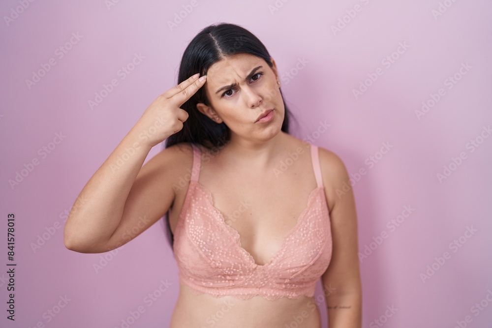 Young hispanic woman wearing pink bra shooting and killing oneself pointing hand and fingers to head like gun, suicide gesture. Young hispanic woman wearing pink bra shooting and killing oneself pointing hand and fingers to head like gun, suicide gesture.