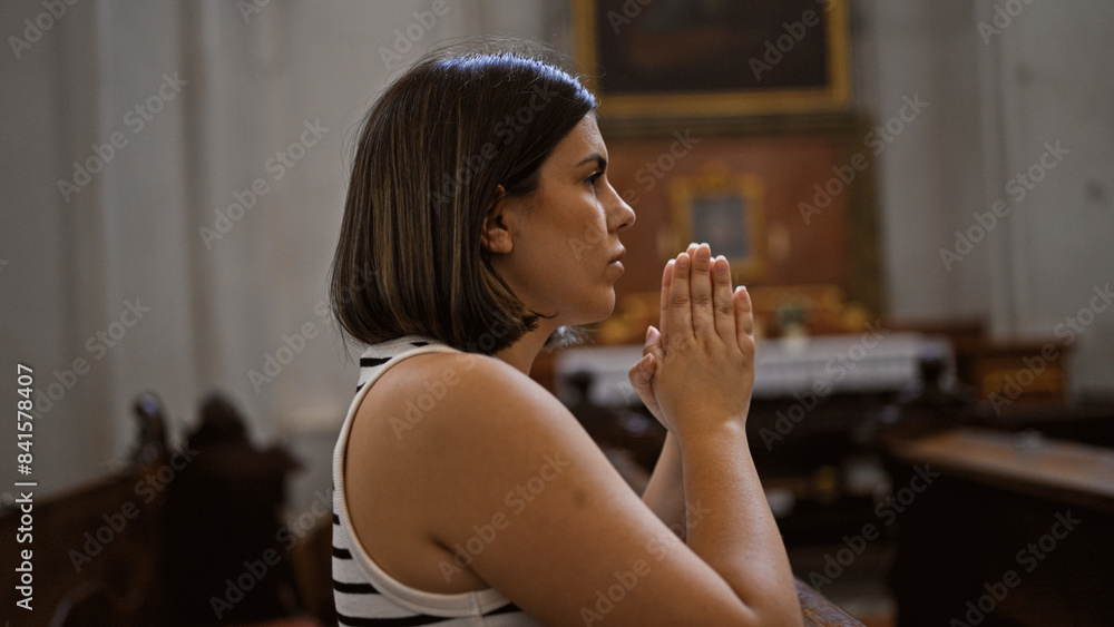 Young beautiful hispanic woman praying on a church bench at Augustinian Church in Vienna Young beautiful hispanic woman praying on a church bench at Augustinian Church in Vienna
