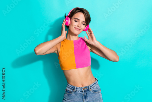 Photo of dreamy pretty woman wear pink orange top closed eyes enjoying music headphones isolated teal color background