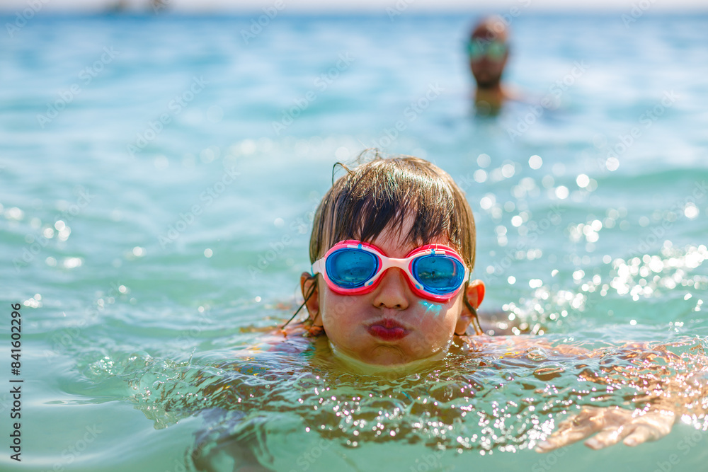 Naklejka premium Little girl wearing goggles, swimming in the warm blue sea