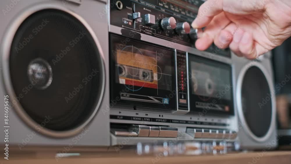 A finger presses the play button on a retro boombox, starting the ...
