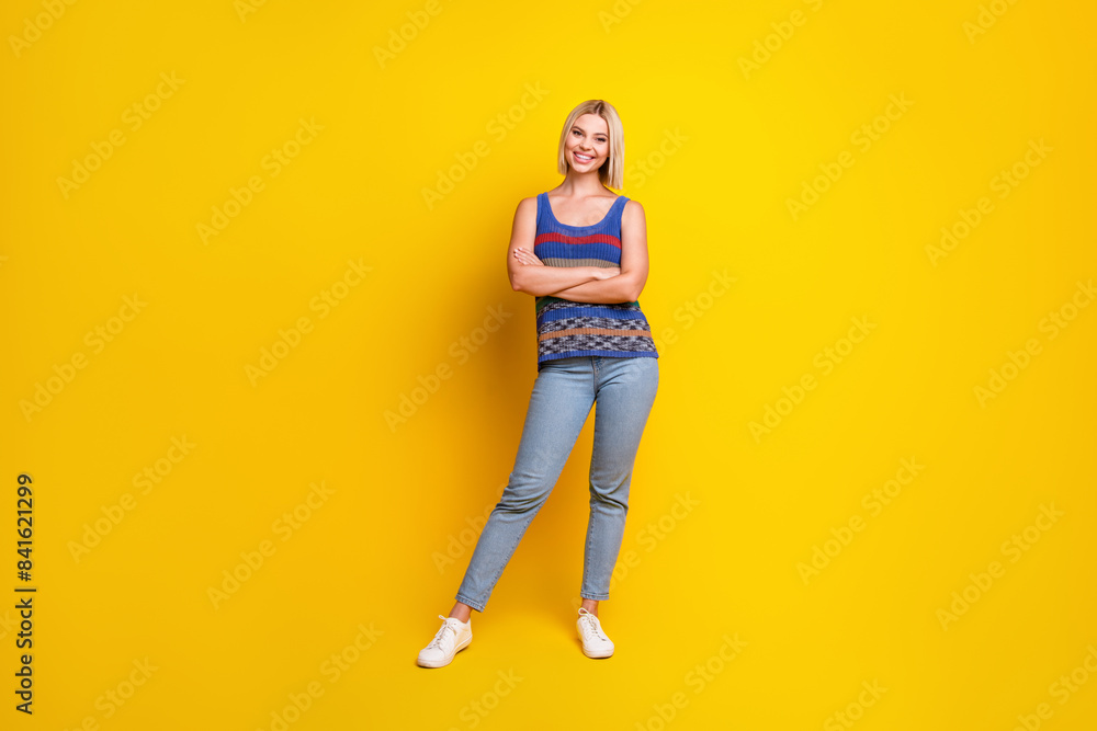 Photo of young optimistic woman student in singlet and jeans posing folded hands apparel brand isolated on yellow color background Photo of young optimistic woman student in singlet and jeans posing folded hands apparel brand isolated on yellow color background
