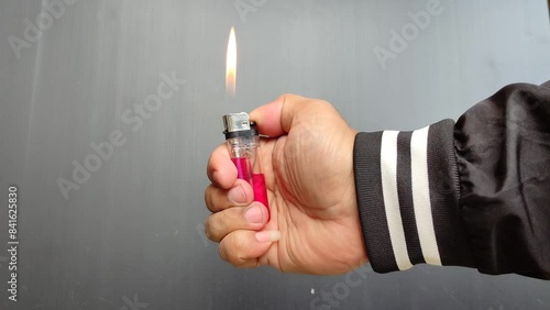 a hand lighting a gas lighter against a dark colored wall photo