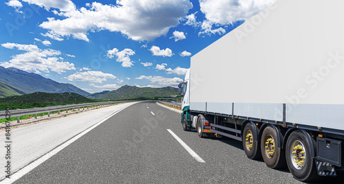 A white truck transports cargo along the highway against the backdrop of a mountain landscape.