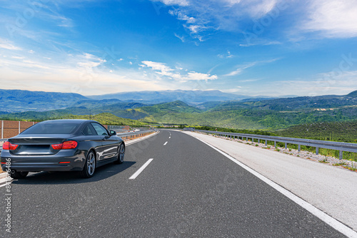 Obraz na płótnie A grey car drives along the highway against the backdrop of rocky mountains on a sunny day. w salonie