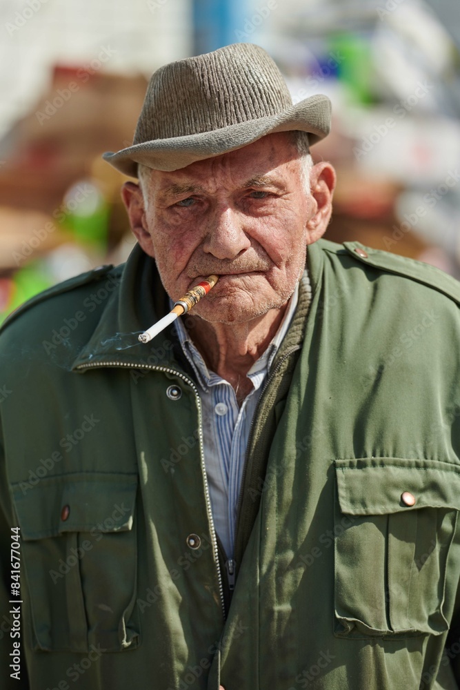 Fototapeta premium Older Man Smoking Cigarette in Dark Green Jacket and Cap