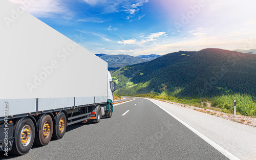 Obraz na płótnie A white truck transports cargo along the highway against the backdrop of a mountain landscape. w salonie