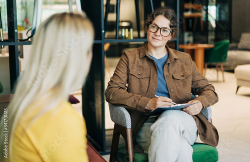 A professional female psychological consultant listens to a client while sitting at her workplace.