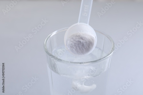 Schilderij op canvas Adding baking soda into glass of water on light grey background, closeup