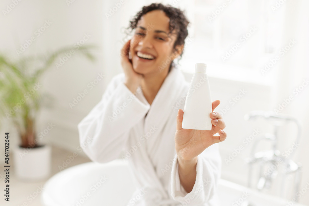 Dispenser bottle with hair shampoo or shower gel, black lady in bathrobe showing hydration lotion cosmetic product with copy space Dispenser bottle with hair shampoo or shower gel, black lady in bathrobe showing hydration lotion cosmetic product with copy space