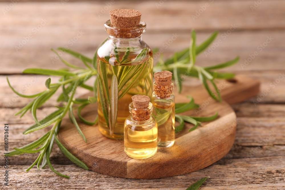 Aromatic essential oils in bottles and rosemary on wooden table, closeup Aromatic essential oils in bottles and rosemary on wooden table, closeup