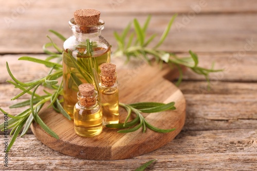 Aromatic essential oils in bottles and rosemary on wooden table, closeup. Space for text