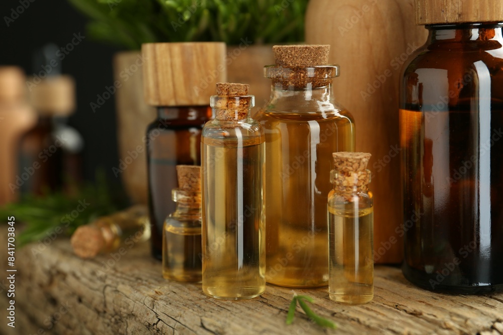 Essential oils in bottles, rosemary on wooden surface, closeup Essential oils in bottles, rosemary on wooden surface, closeup