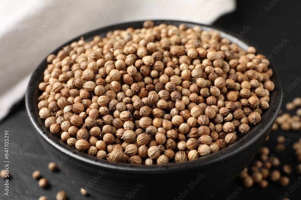 Dried coriander seeds in bowl on dark gray table, closeup
