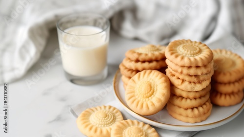 A plate of freshly baked shortbread cookies with a glass of milk on a white tabletop.