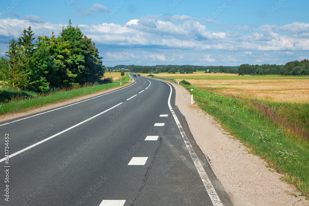 Asphalt road next to wheat fields against a blue sky and clouds in the Riga suburbs, Latvia Asphalt road next to wheat fields against a blue sky and clouds in the Riga suburbs, Latvia
