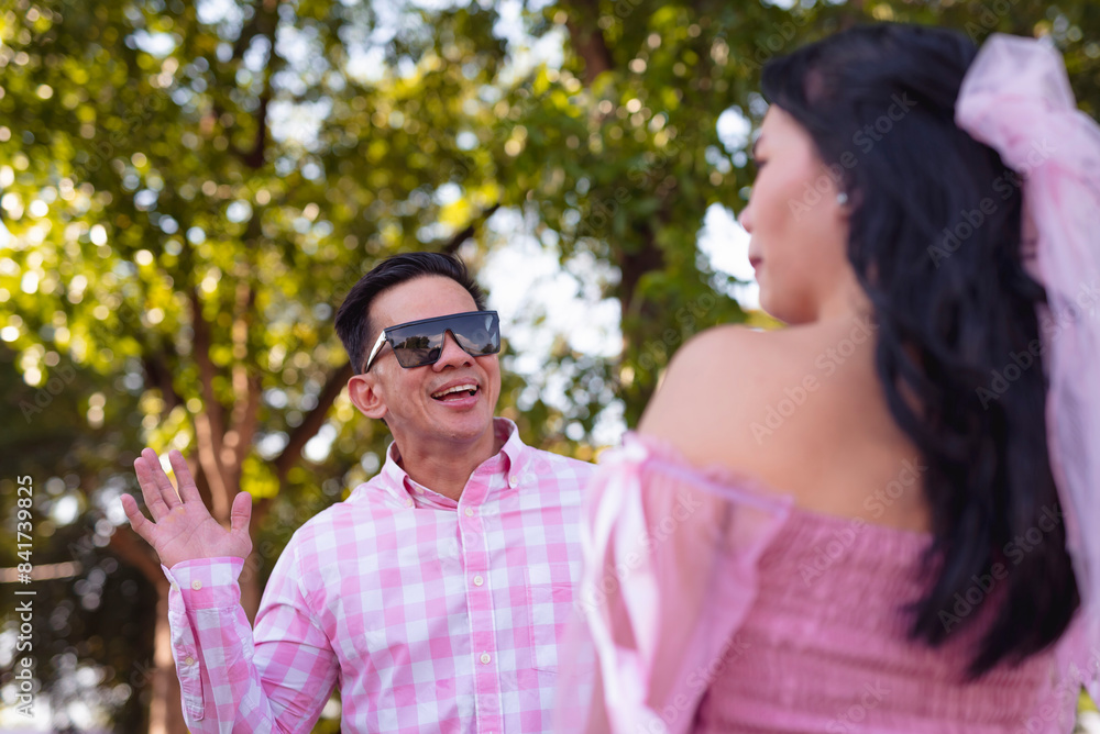 A handsome youthful asian man tries to make a joke to his daughter who does not get it. Both wearing pink clothes celebrating Father's Day outdoors at the park. A handsome youthful asian man tries to make a joke to his daughter who does not get it. Both wearing pink clothes celebrating Father's Day outdoors at the park.