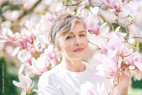 Spring close up portrait of beautiful 55 - 60 year old woman posing with magnolia tree