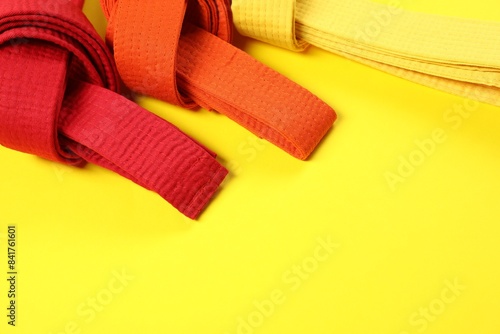 Colorful karate belts on yellow background, flat lay. Space for text